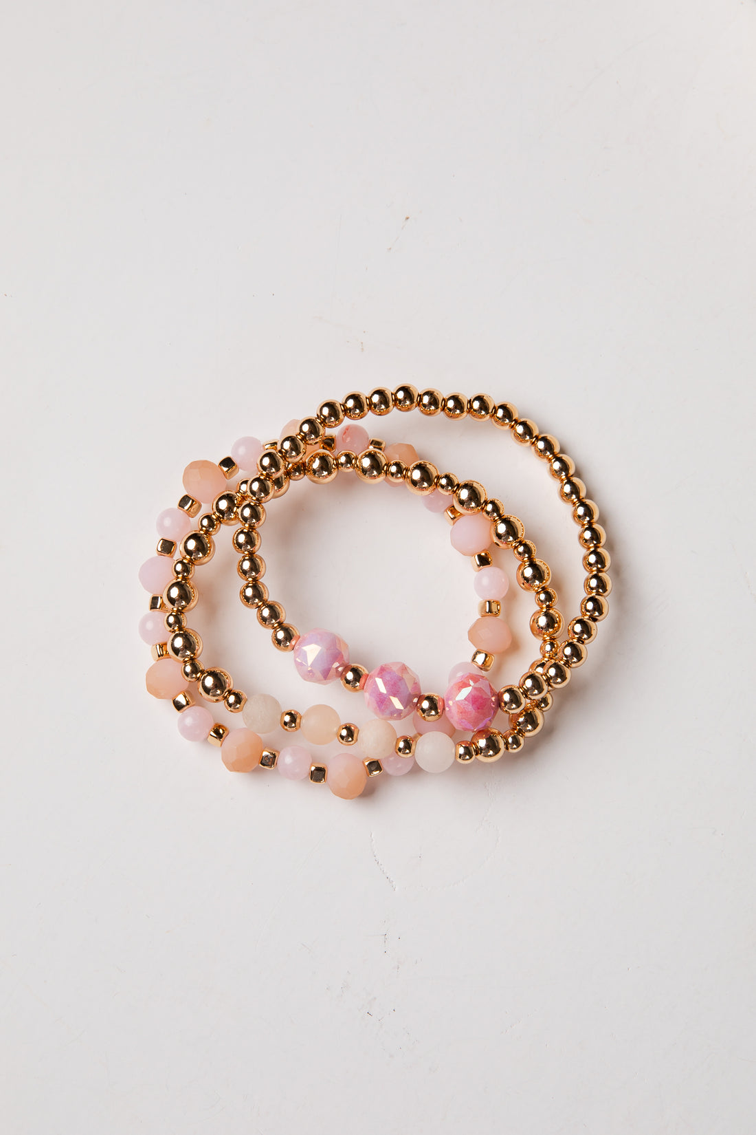 Set of three beaded bracelets with pink and gold beads on a white background