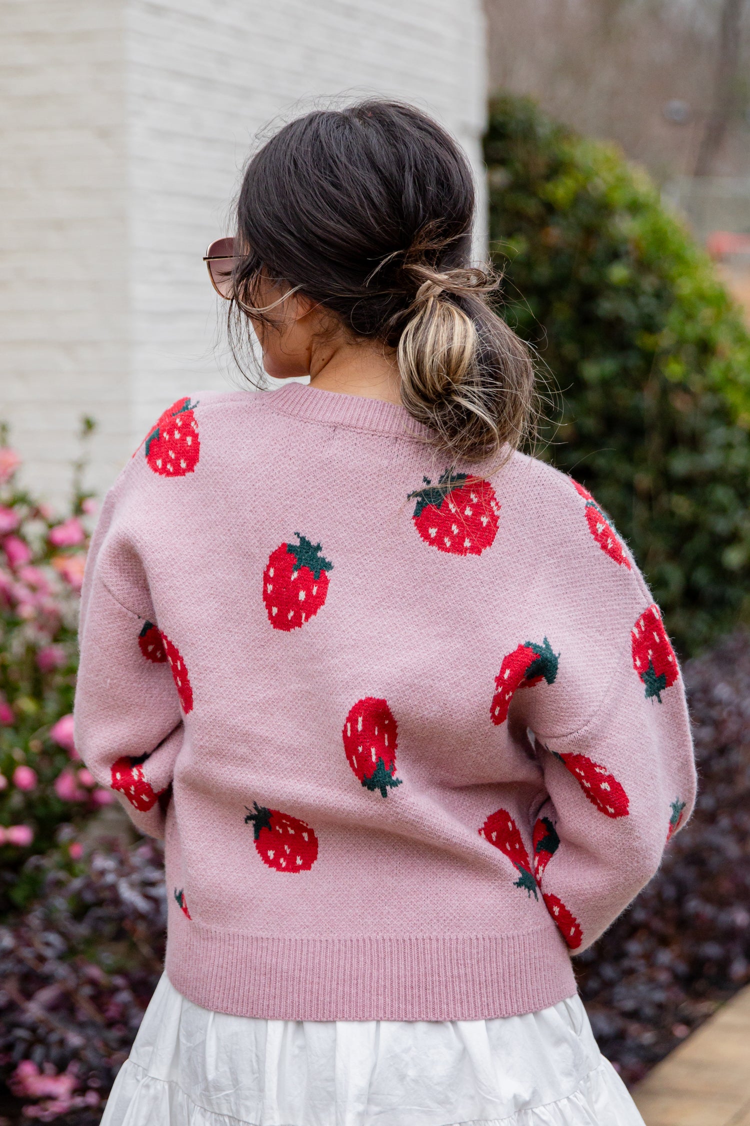 Person wearing a pink sweater with strawberry patterns outdoors.