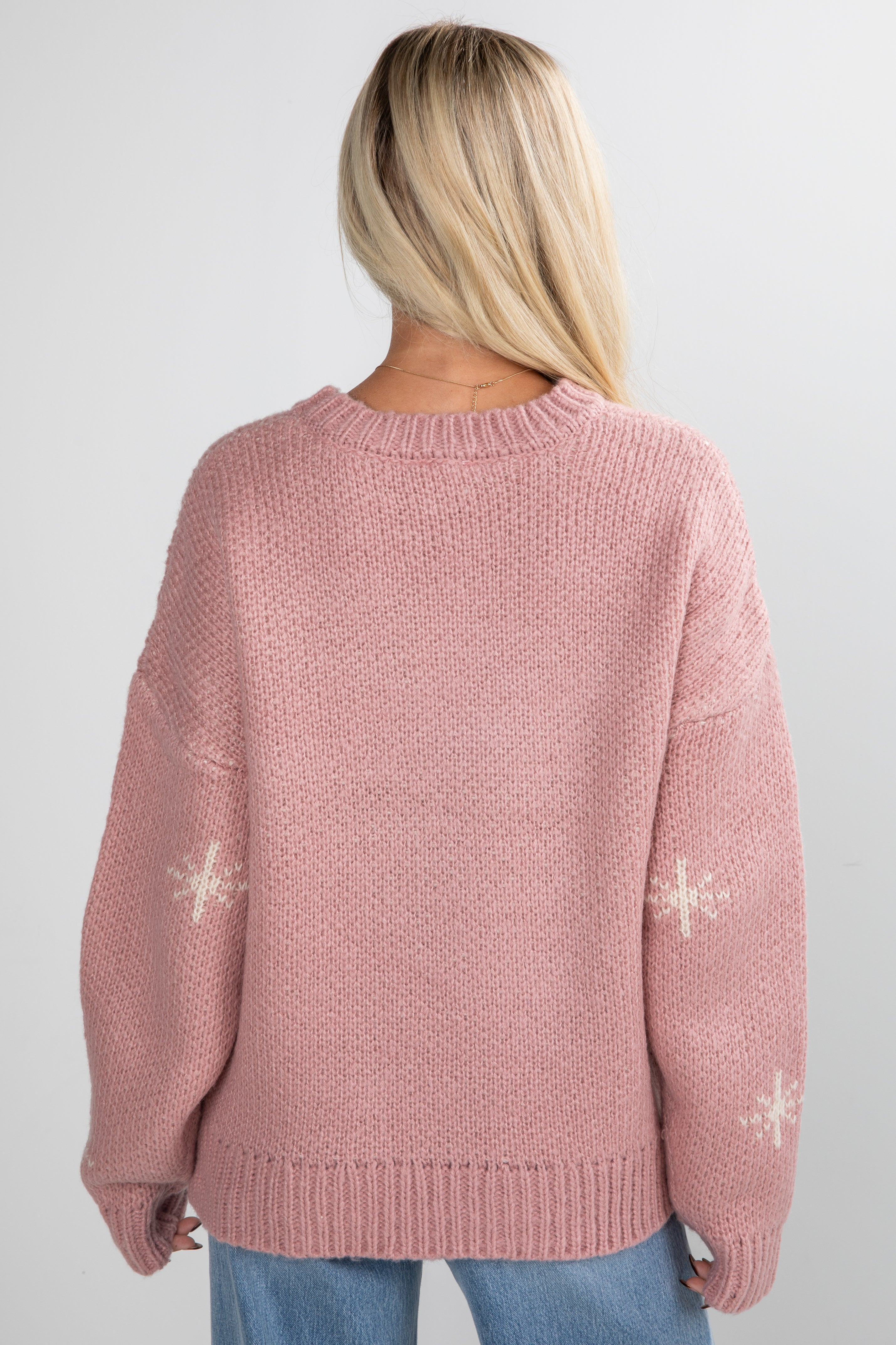 Pink knitted sweater with snowflake patterns worn by a person on a white background