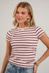 A woman wearing a light pink short-sleeve t-shirt with dark red horizontal stripes, paired with blue jeans, against a white paneled wall.