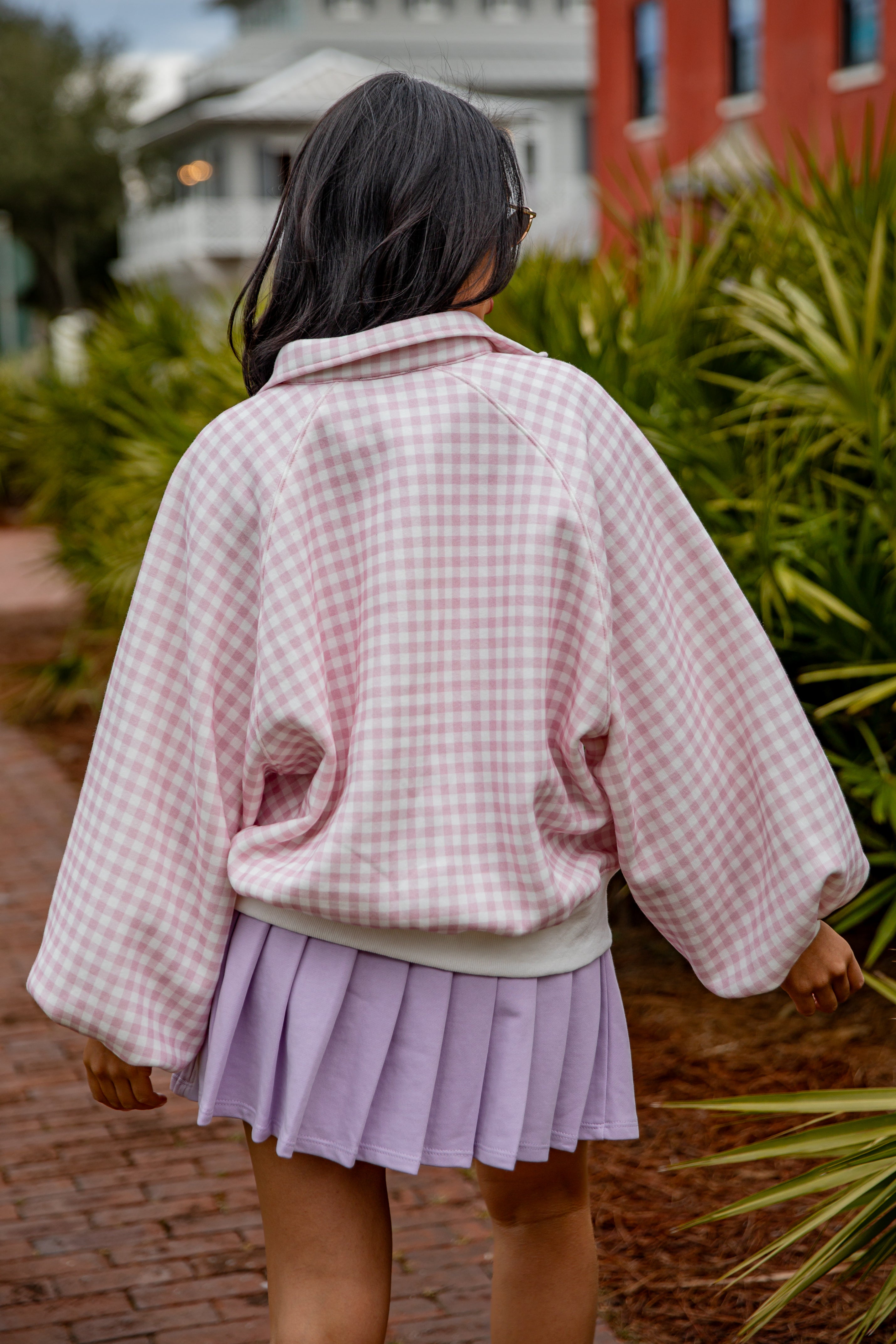 Person wearing a pink checkered jacket and purple skirt walking outdoors.