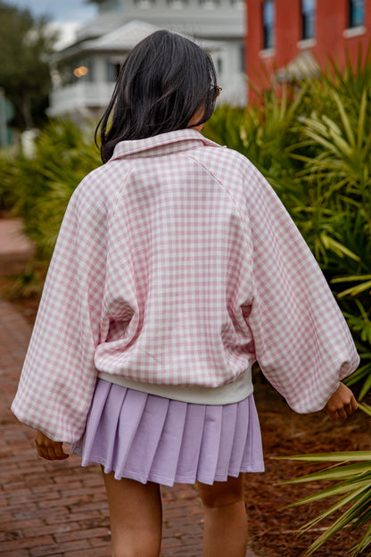 Person wearing a pink checkered jacket and purple skirt walking outdoors.