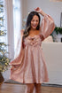 Woman in a pink dress with a bow standing in a living room with Christmas decorations.