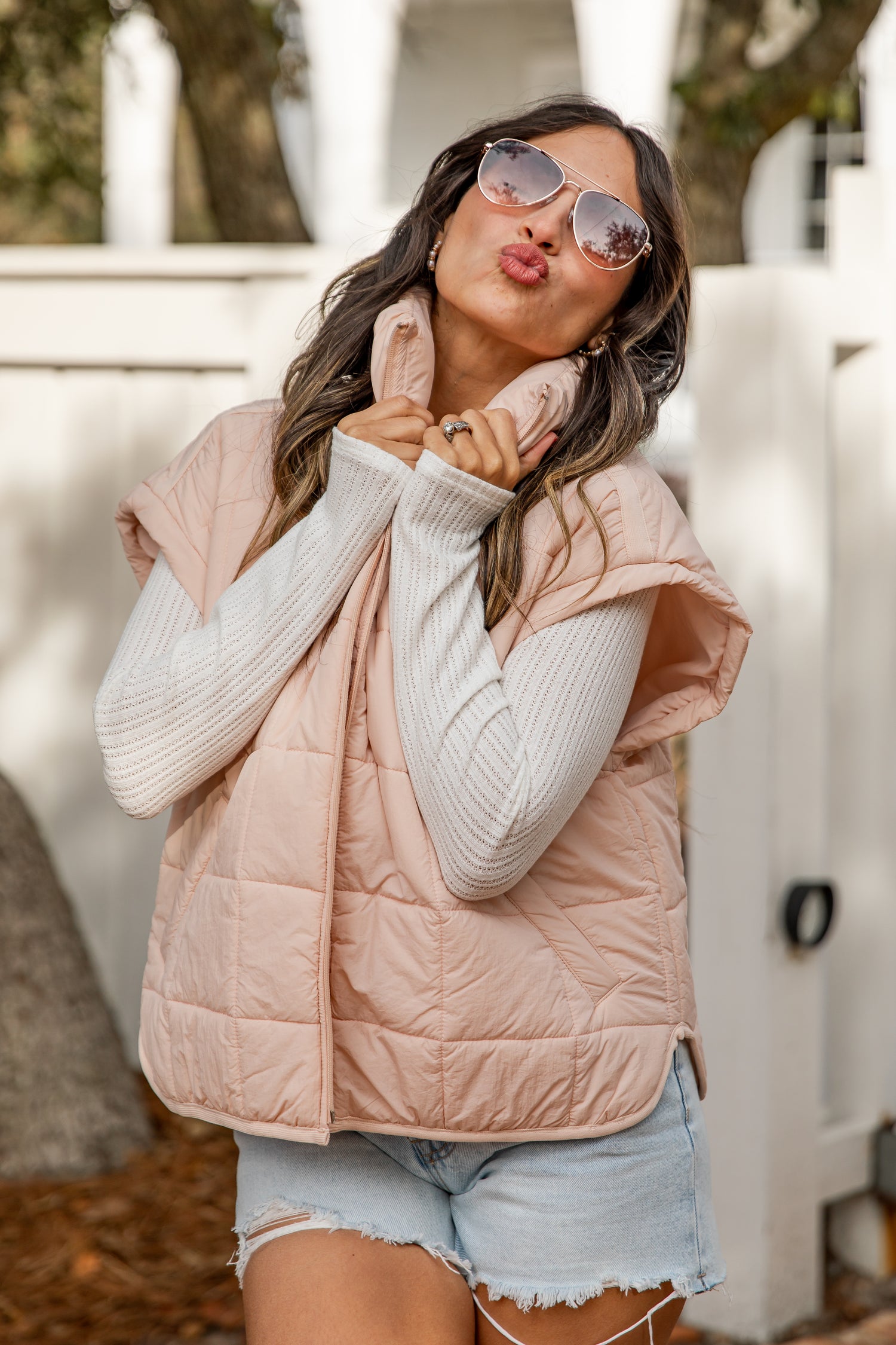 Woman wearing a pink puffer vest and sunglasses, posing outdoors.