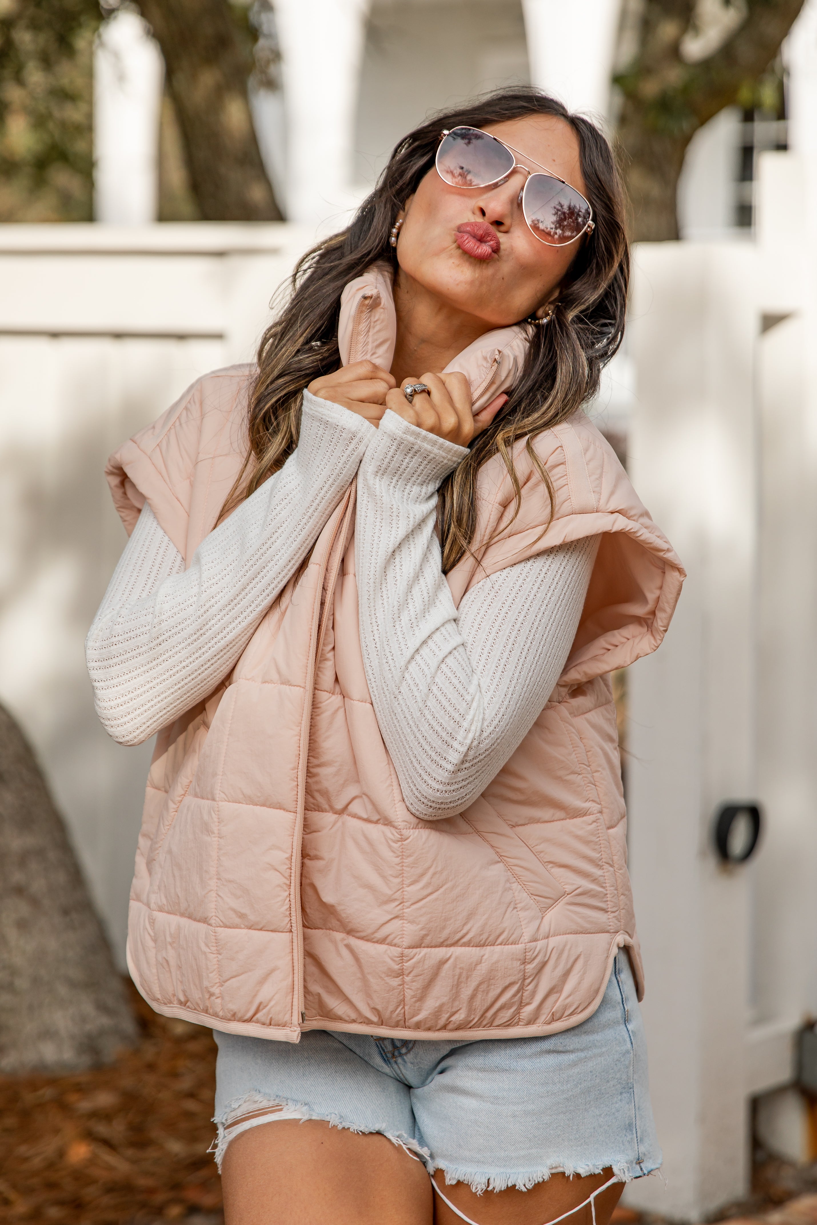 Woman wearing a pink puffer vest and sunglasses, posing outdoors.