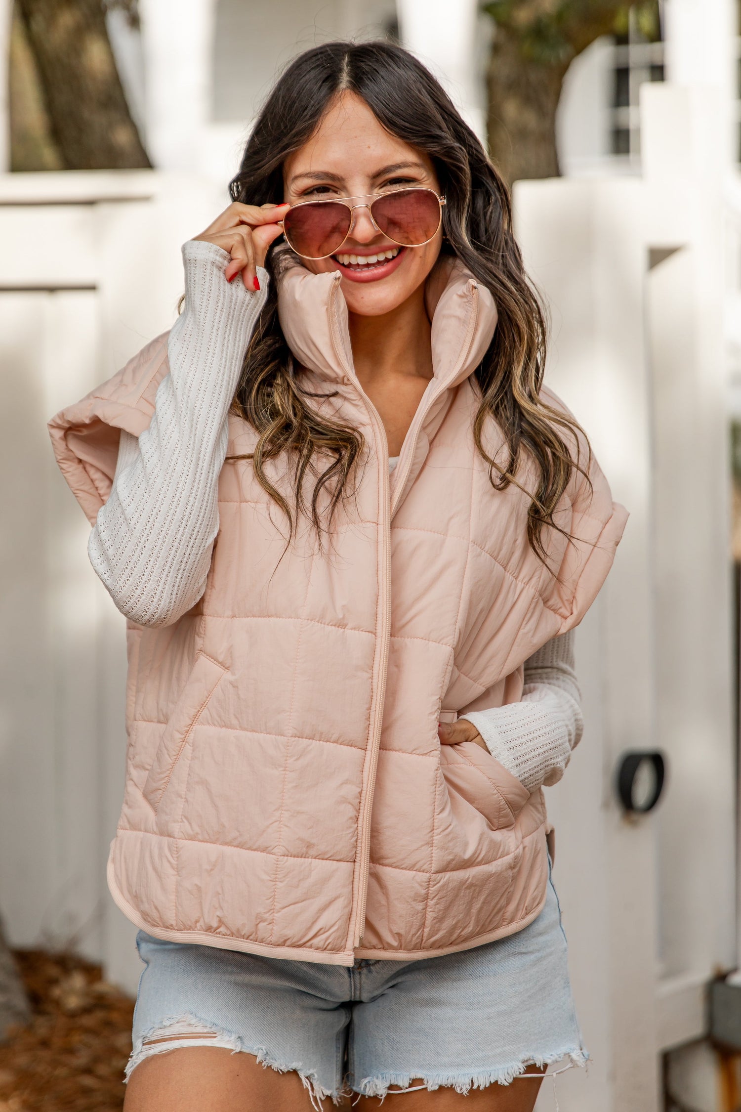 Woman wearing a pink puffer vest and denim shorts outdoors.