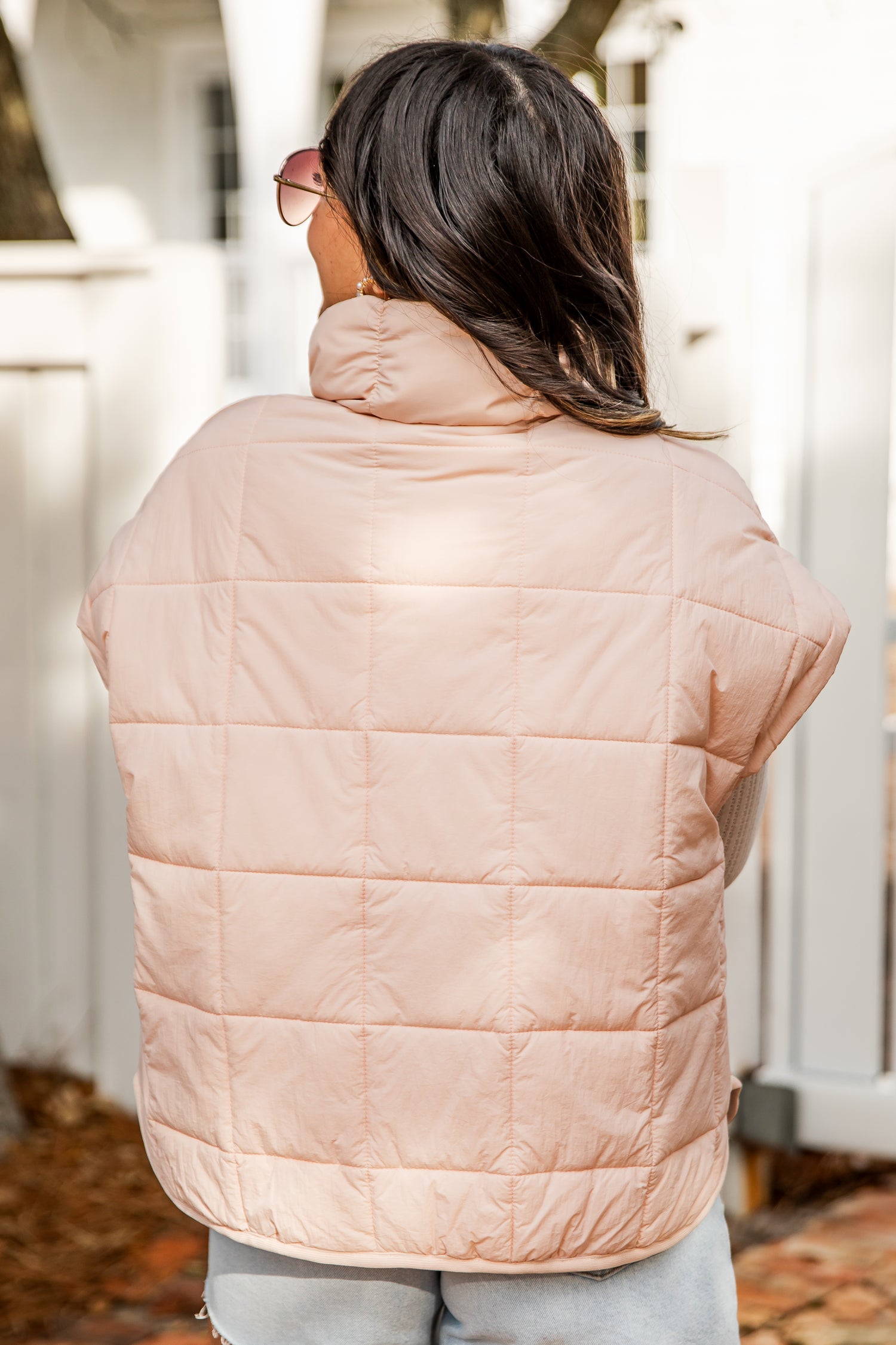 Person wearing a light pink puffer vest outdoors.