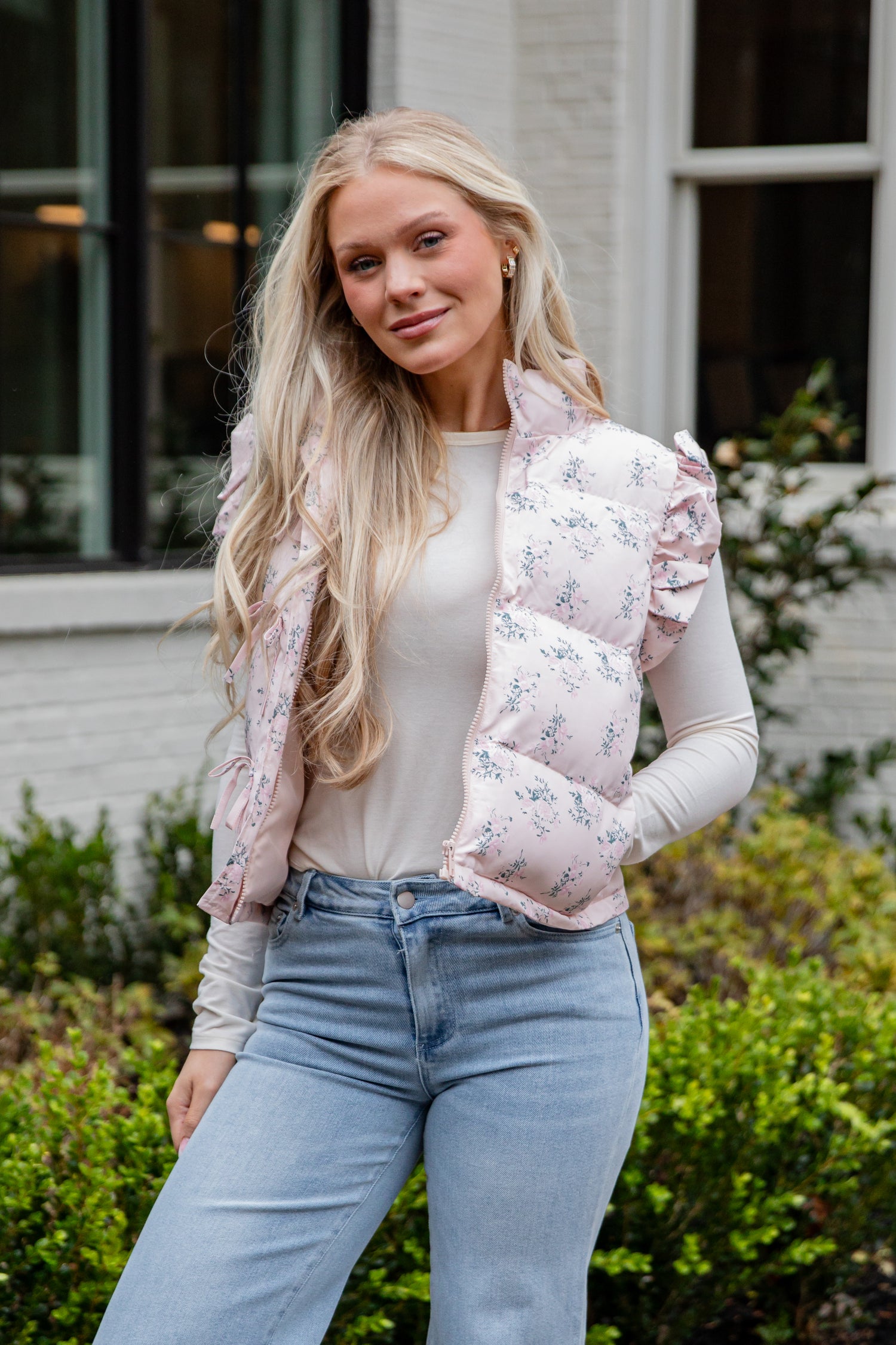 Woman wearing a floral puffer vest over a white shirt and blue jeans, standing outdoors.