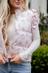 Woman wearing a light pink floral puffer vest over a white long-sleeve shirt with a blurred outdoor background.