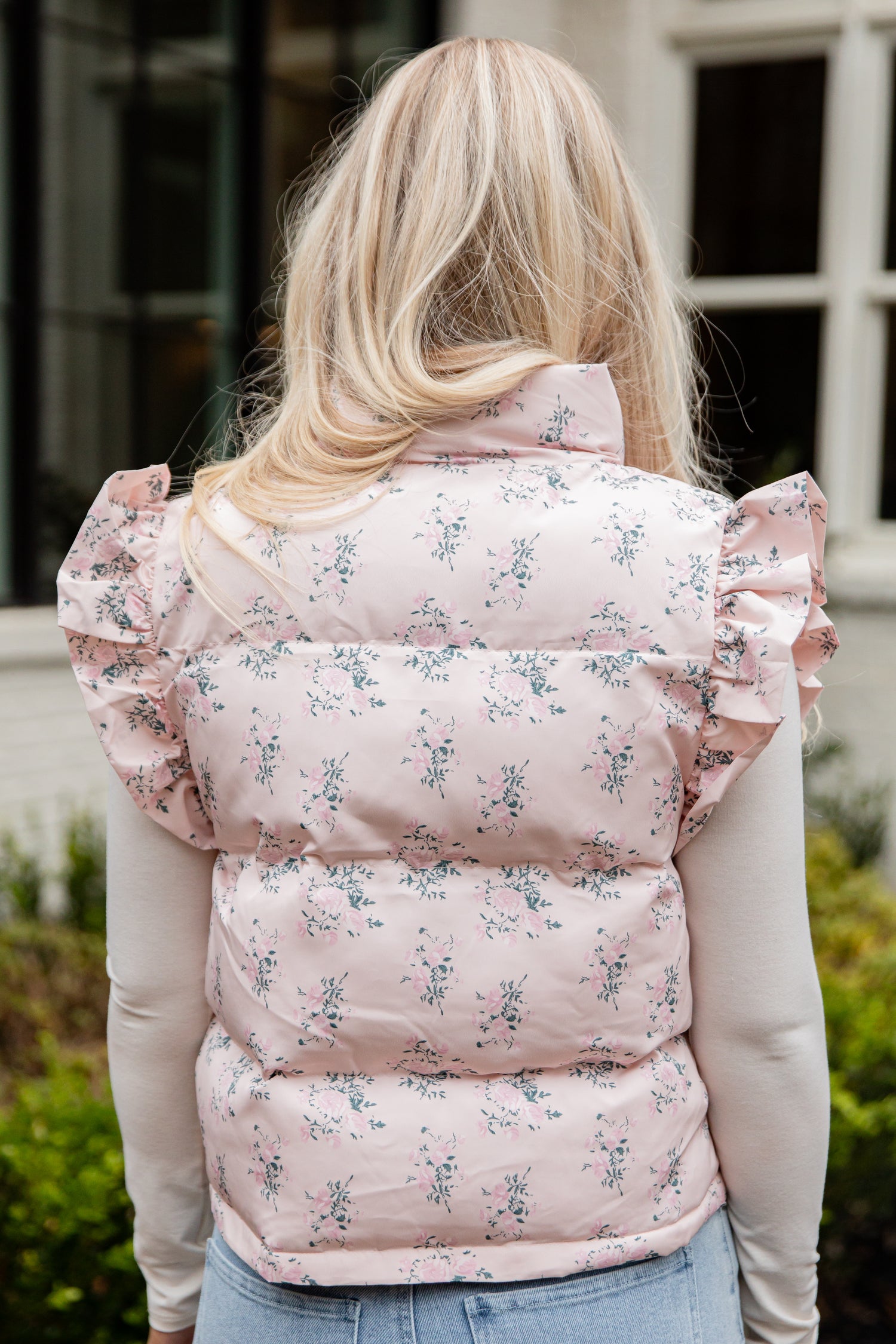 Person wearing a pink floral puffer vest outdoors.