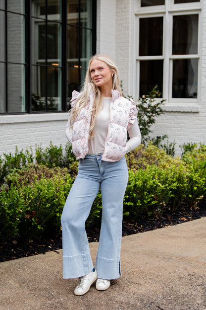 Woman wearing a white puffer vest and light blue jeans standing outdoors.