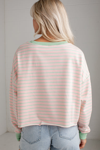 A woman viewed from behind wearing a light pink and white striped long-sleeve crop top with sage green ribbed trim, paired with light blue jeans.