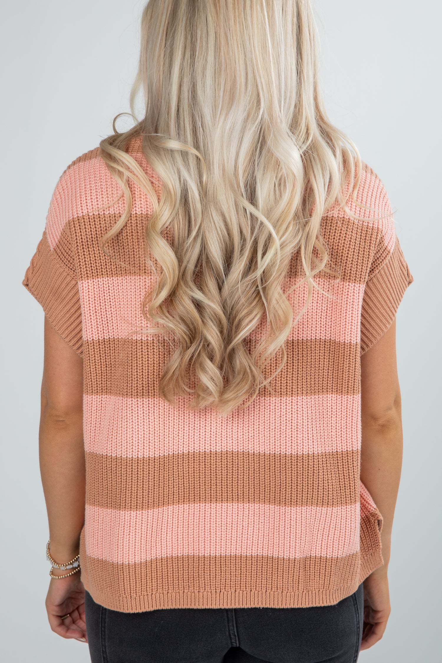 Person wearing a pink and brown striped sweater against a white background