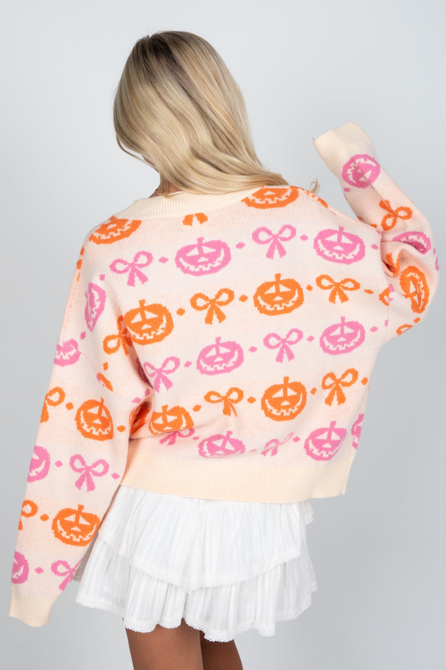 Person wearing a colorful sweater with pumpkins and bows on a plain background