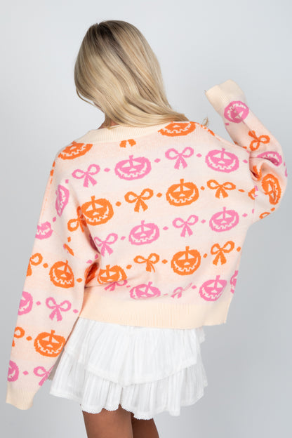Person wearing a colorful sweater with pumpkins and bows on a plain background