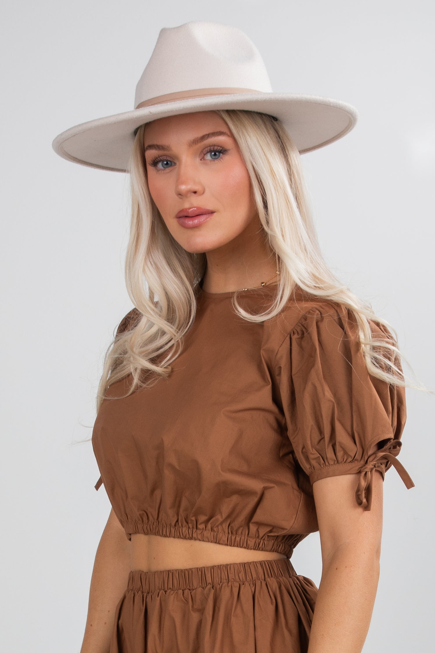 Woman wearing a brown top and beige hat against a white background