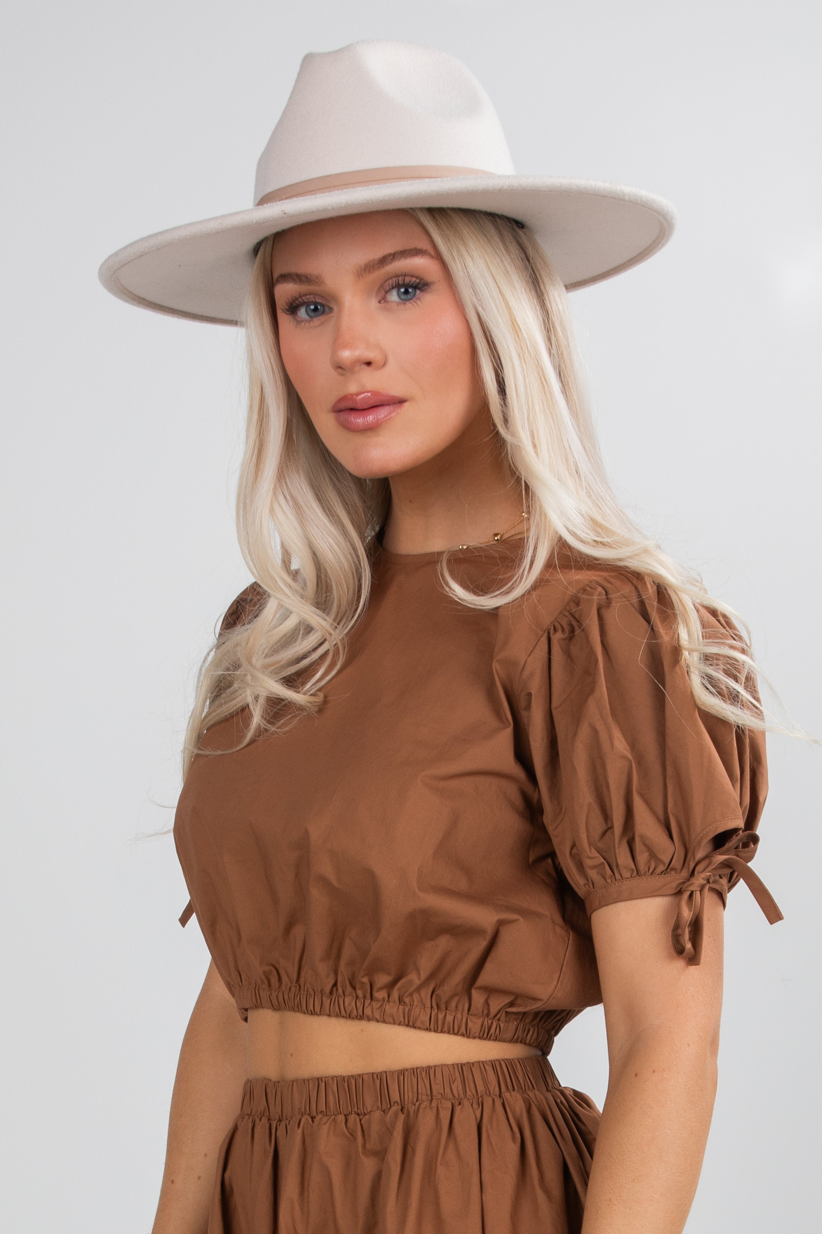 Woman wearing a brown top and beige hat against a white background