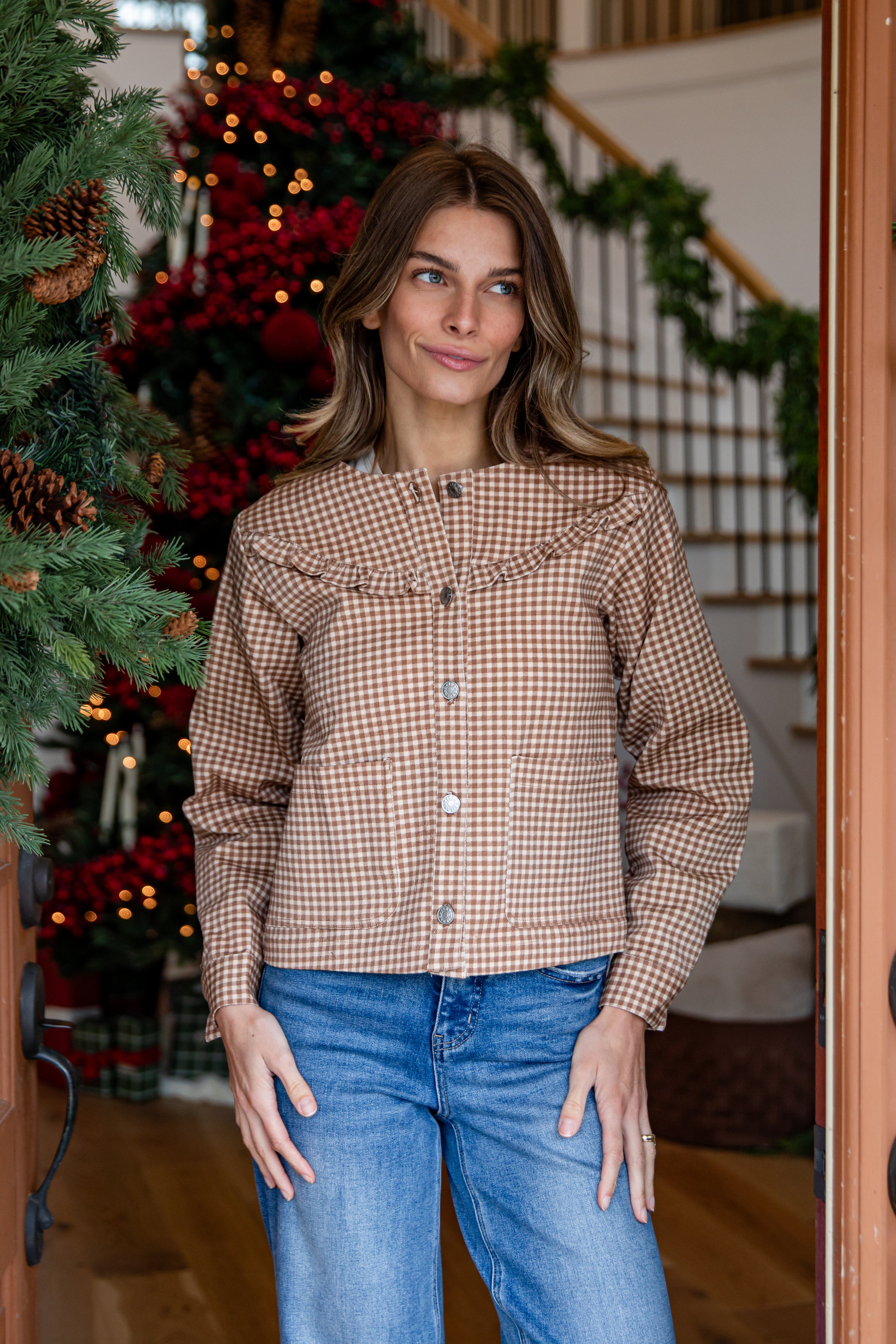 Woman wearing a plaid shirt and jeans standing in a decorated room with Christmas trees.