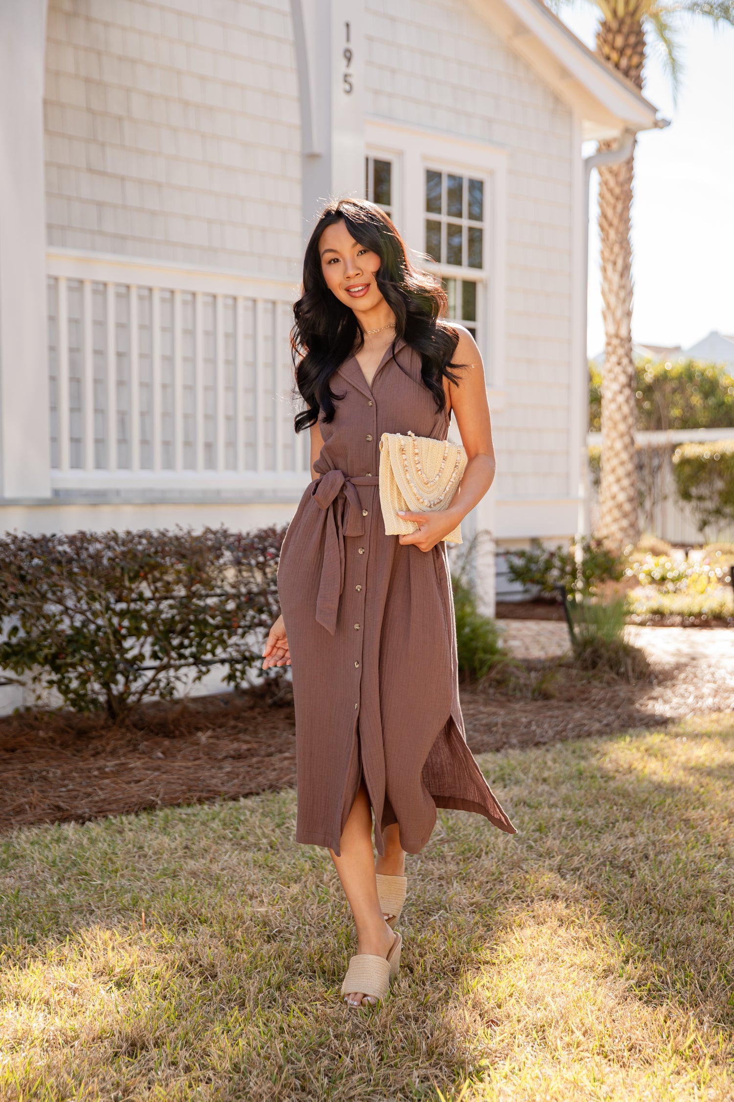 Woman in a brown dress standing in front of a house with a palm tree in the background