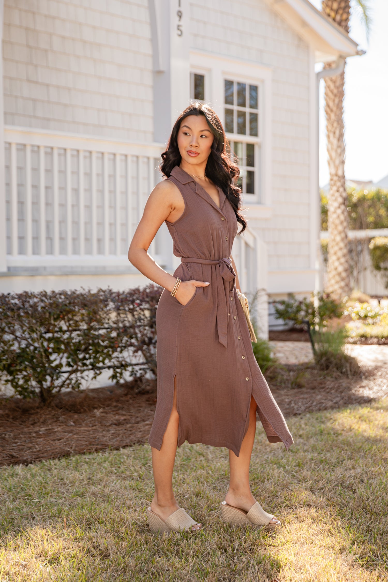 Woman in a brown dress standing outdoors in front of a house.