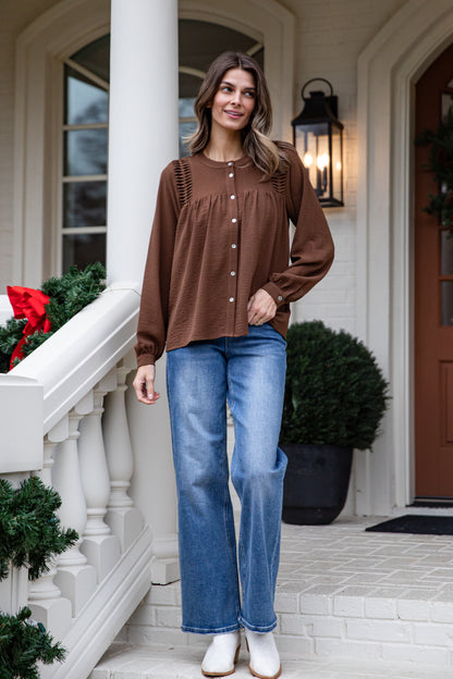 Woman wearing a brown top and blue jeans standing on a porch with holiday decorations.