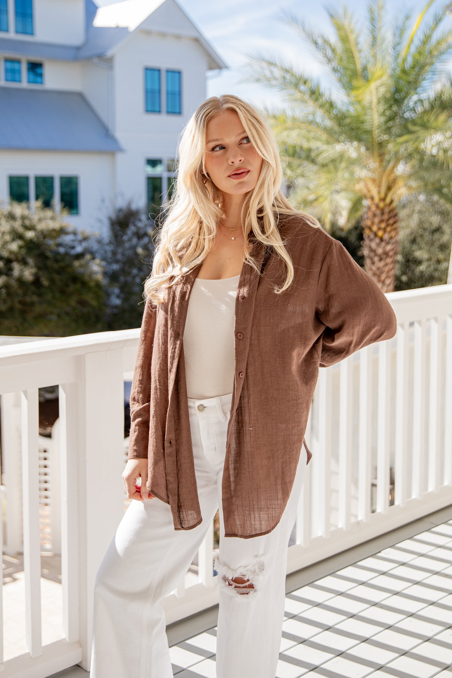 Woman standing on a balcony with a house and palm trees in the background
