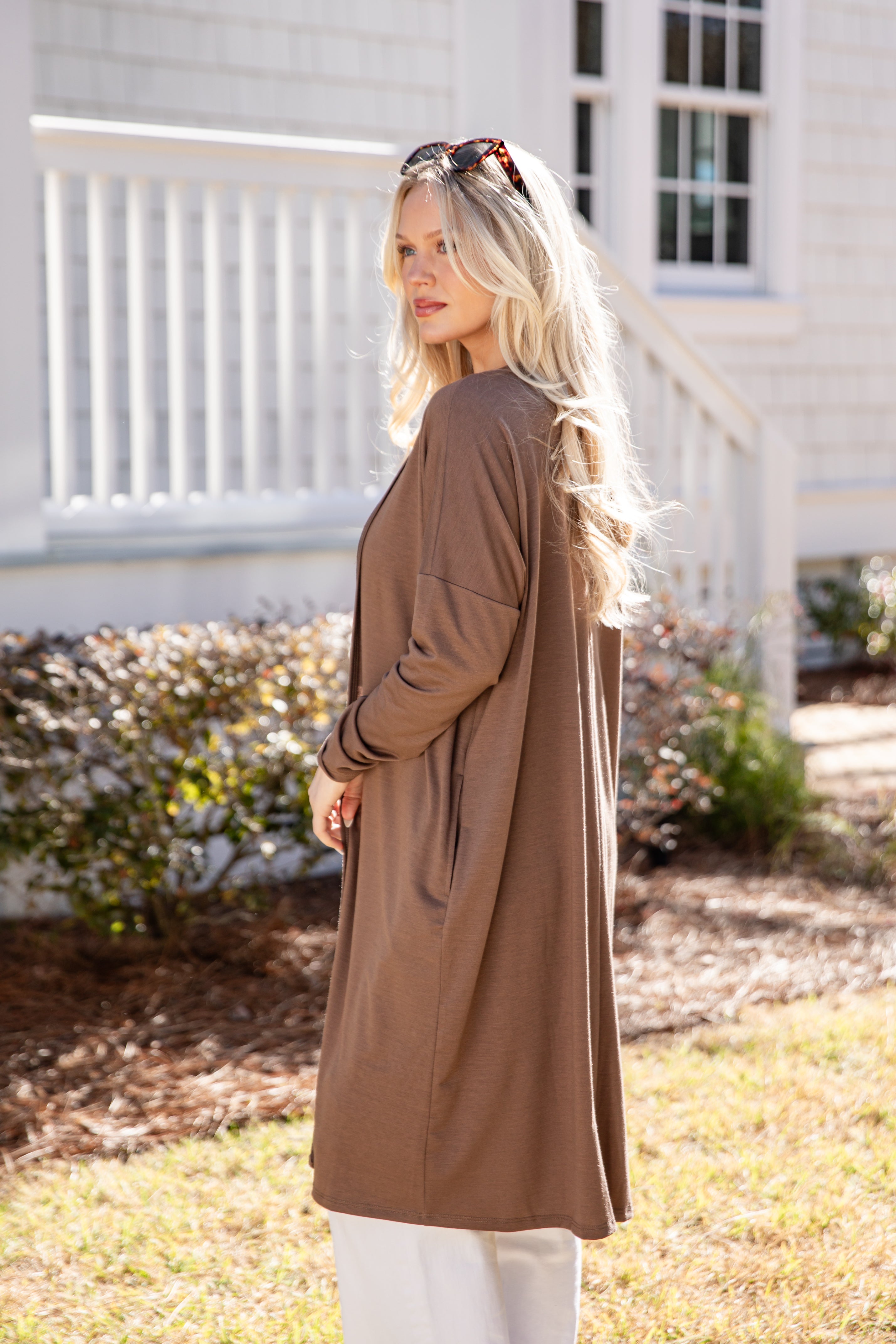 Woman wearing a long brown coat standing outdoors near a house.