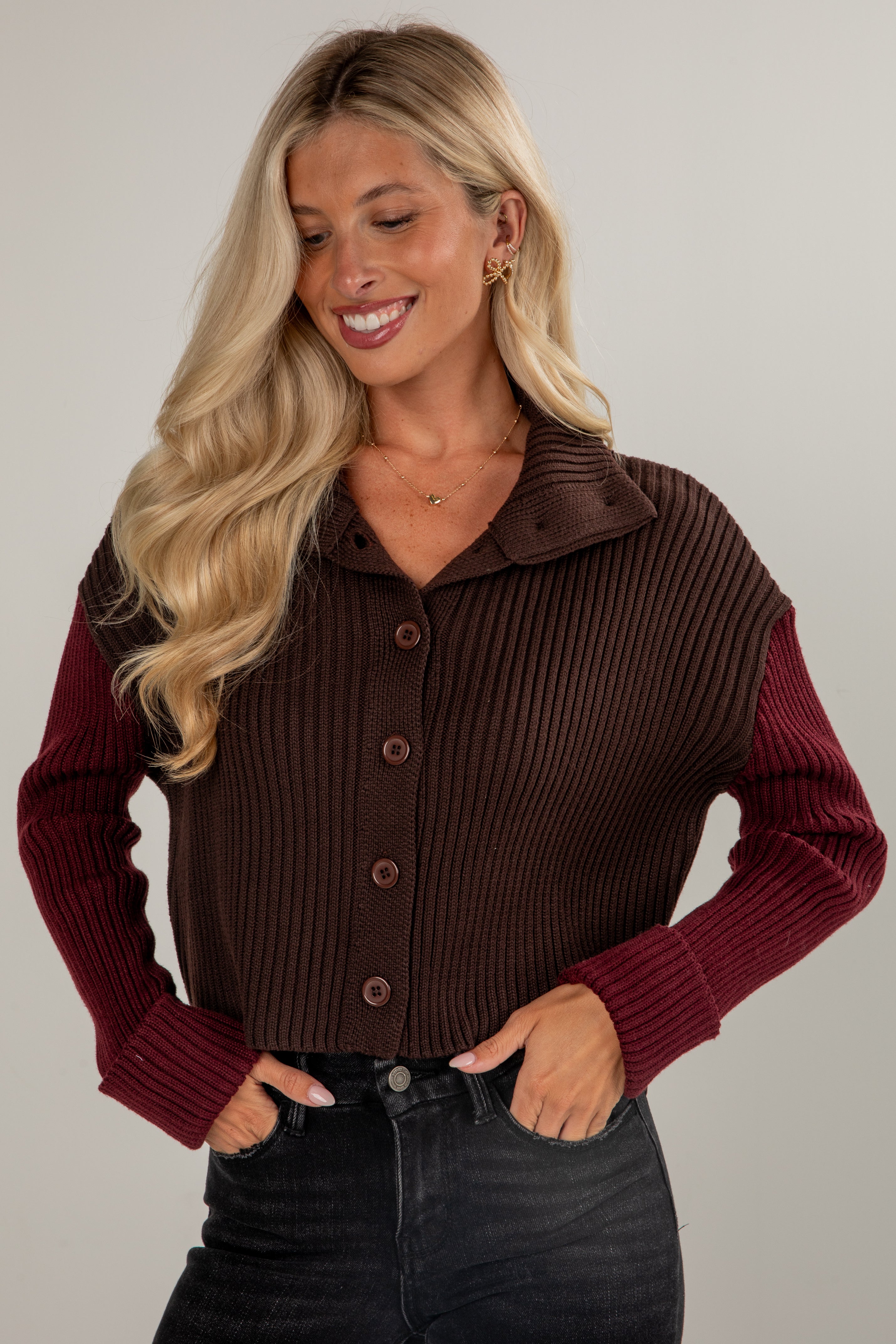 Woman wearing a brown ribbed sweater with burgundy sleeves on a plain background