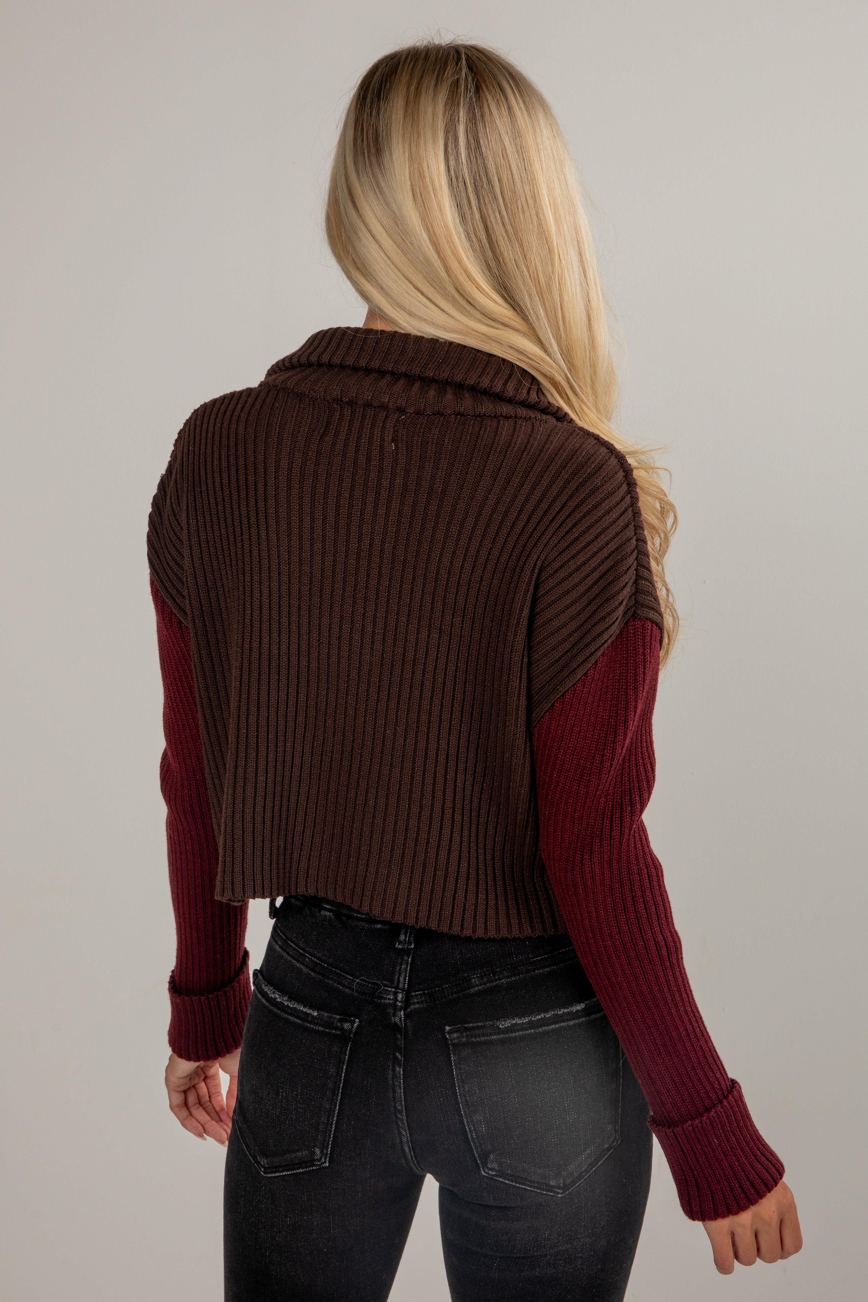 Person wearing a brown and burgundy ribbed sweater vest on a plain background