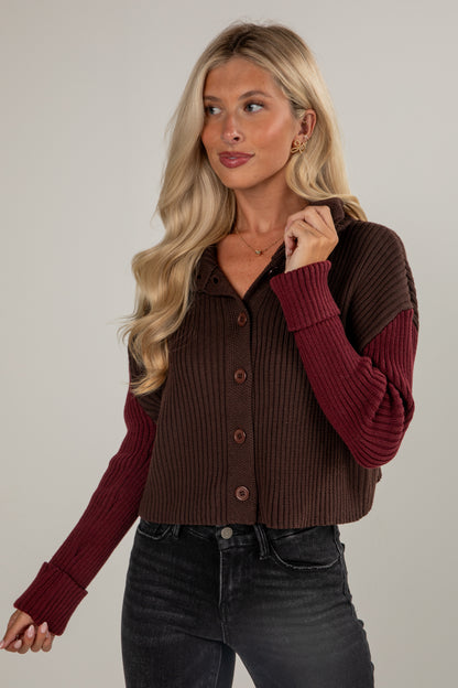 Woman wearing a two-tone cardigan with maroon sleeves and a brown body on a plain background