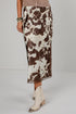 A model is shown from the waist down wearing a brown and white cow-print midi skirt with a lace hem, paired with cream-colored pointed-toe ankle boots.