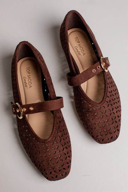 A pair of brown perforated Mary Jane flats with gold-tone buckle straps, shown from a top-down angle on a light gray background. The brand name &