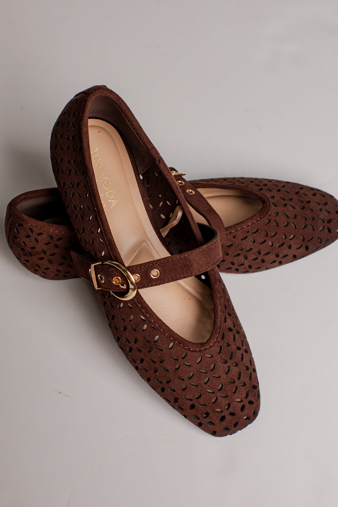 A pair of dark brown Mary Jane shoes with a textured, perforated upper and a gold-tone buckle strap, displayed on a light gray background.