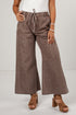 A model wearing wide-leg brown corduroy pants with a drawstring waist, styled with a white top and brown heeled sandals against a light gray studio background.