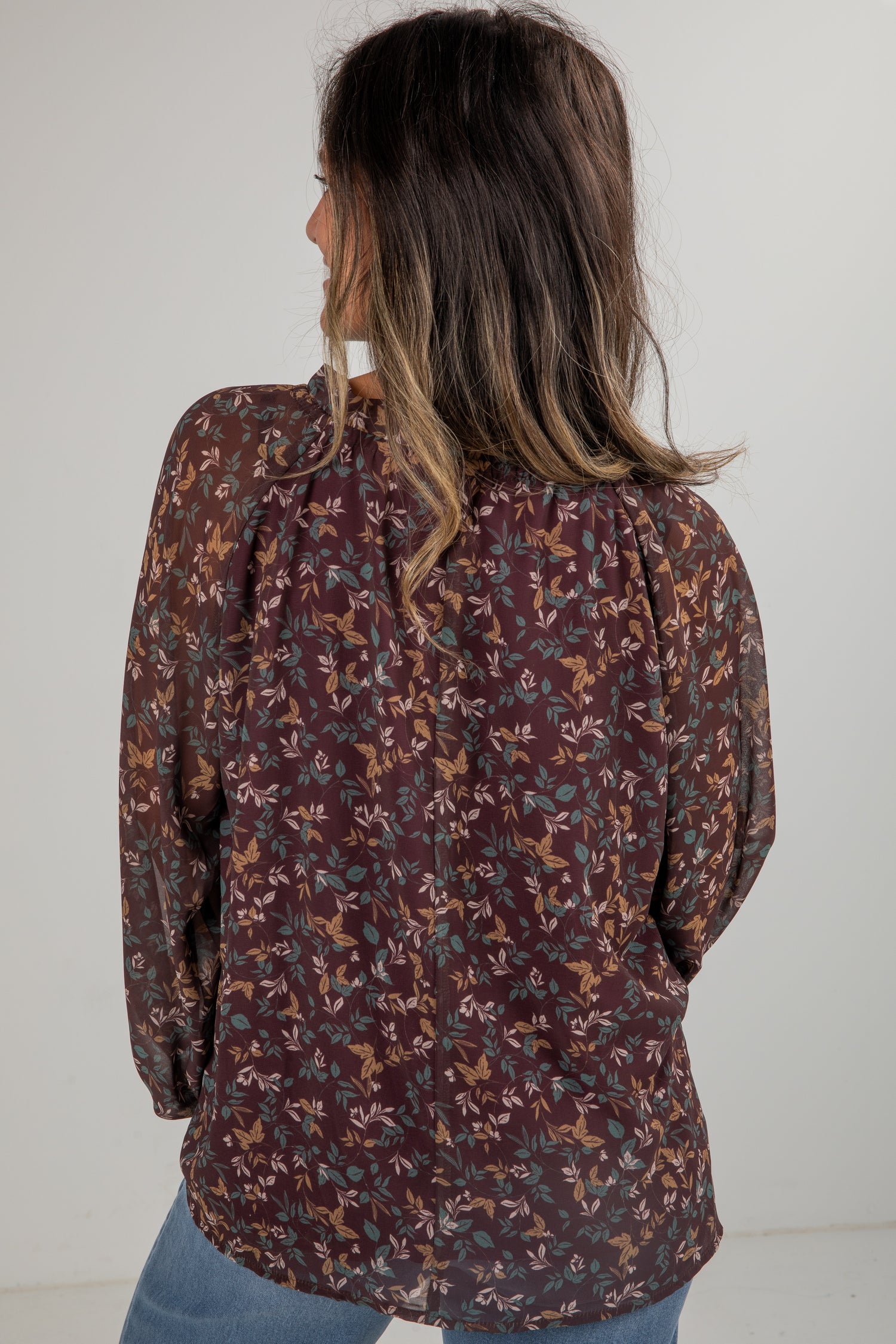 Woman wearing a patterned blouse with long sleeves against a plain background