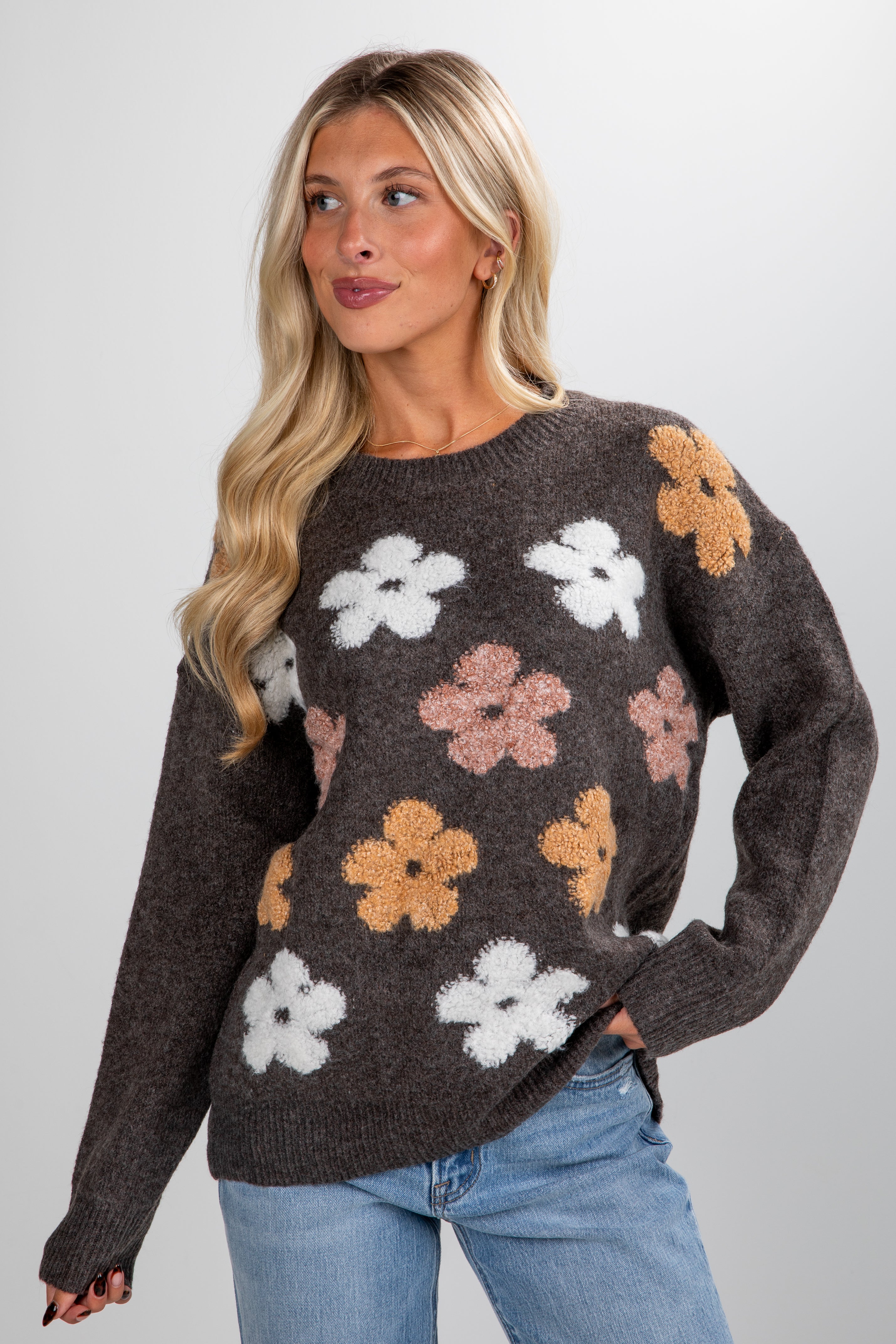 Woman wearing a dark brown sweater with floral patterns on a plain background