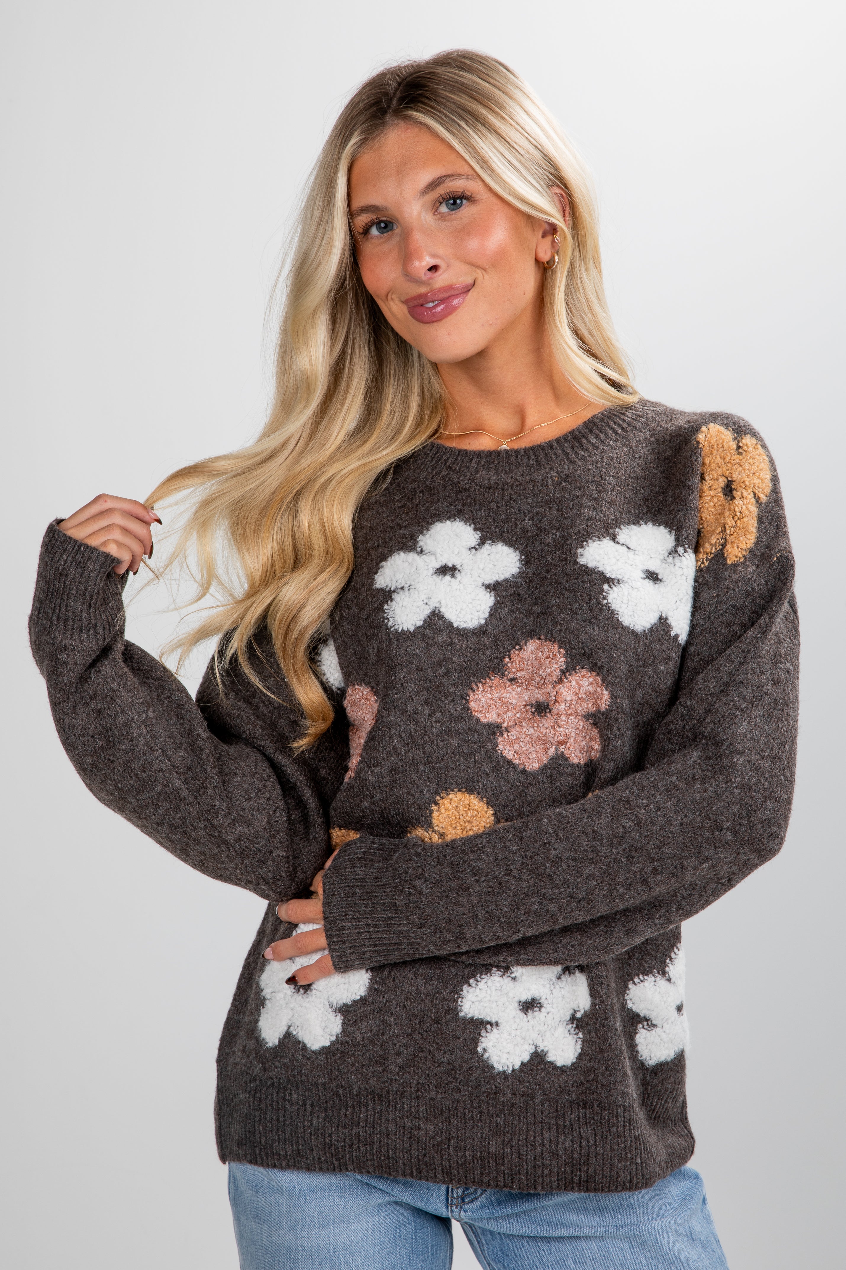 Woman wearing a brown sweater with floral patterns on a plain background