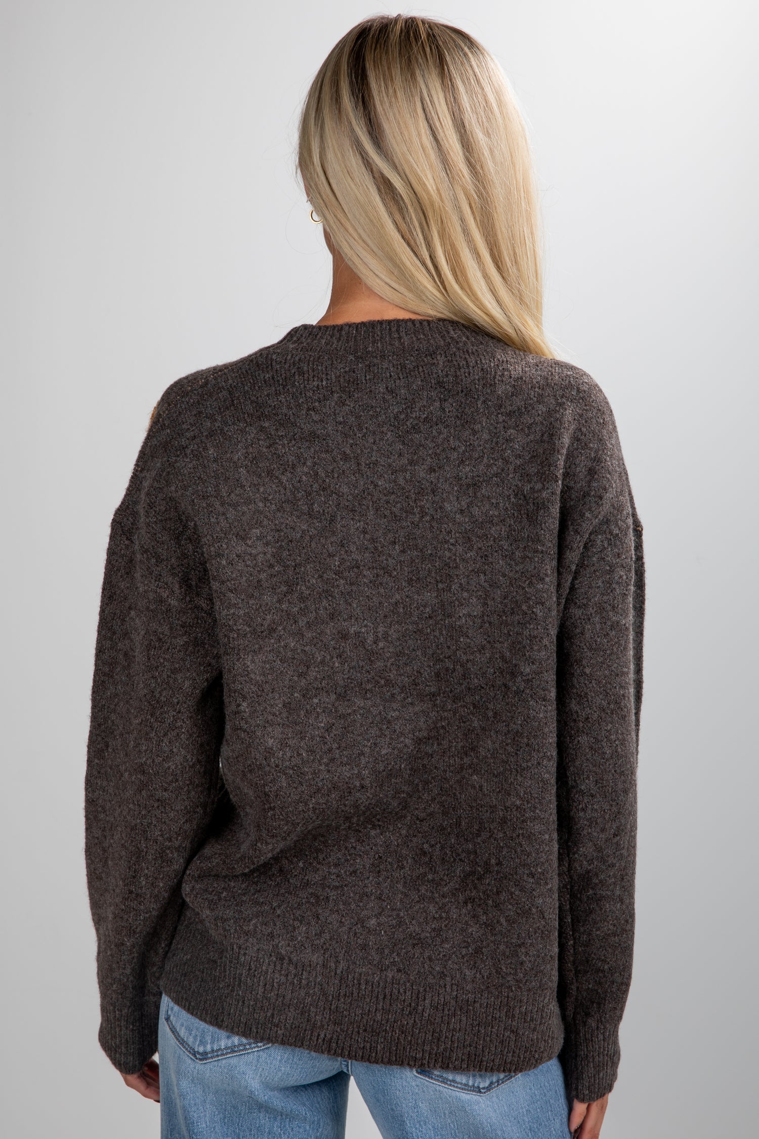 Person wearing a brown sweater and blue jeans on a plain background