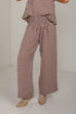 A person wearing brown and beige gingham wide-leg pants with a smocked elastic waist, paired with beige pointed-toe heeled boots, photographed in a plain studio corner.