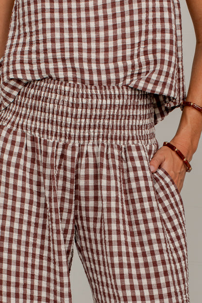 Close-up of a person wearing a brown and white gingham check romper with an elastic waistband and side pockets, paired with a matching top.