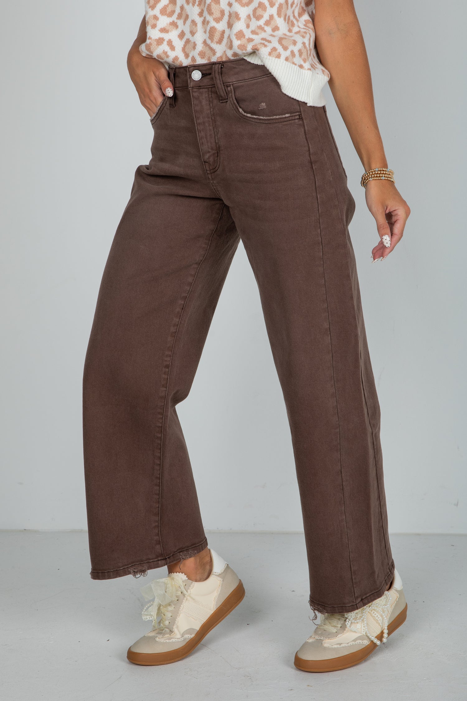Person wearing brown wide-leg jeans and white sneakers on a plain background