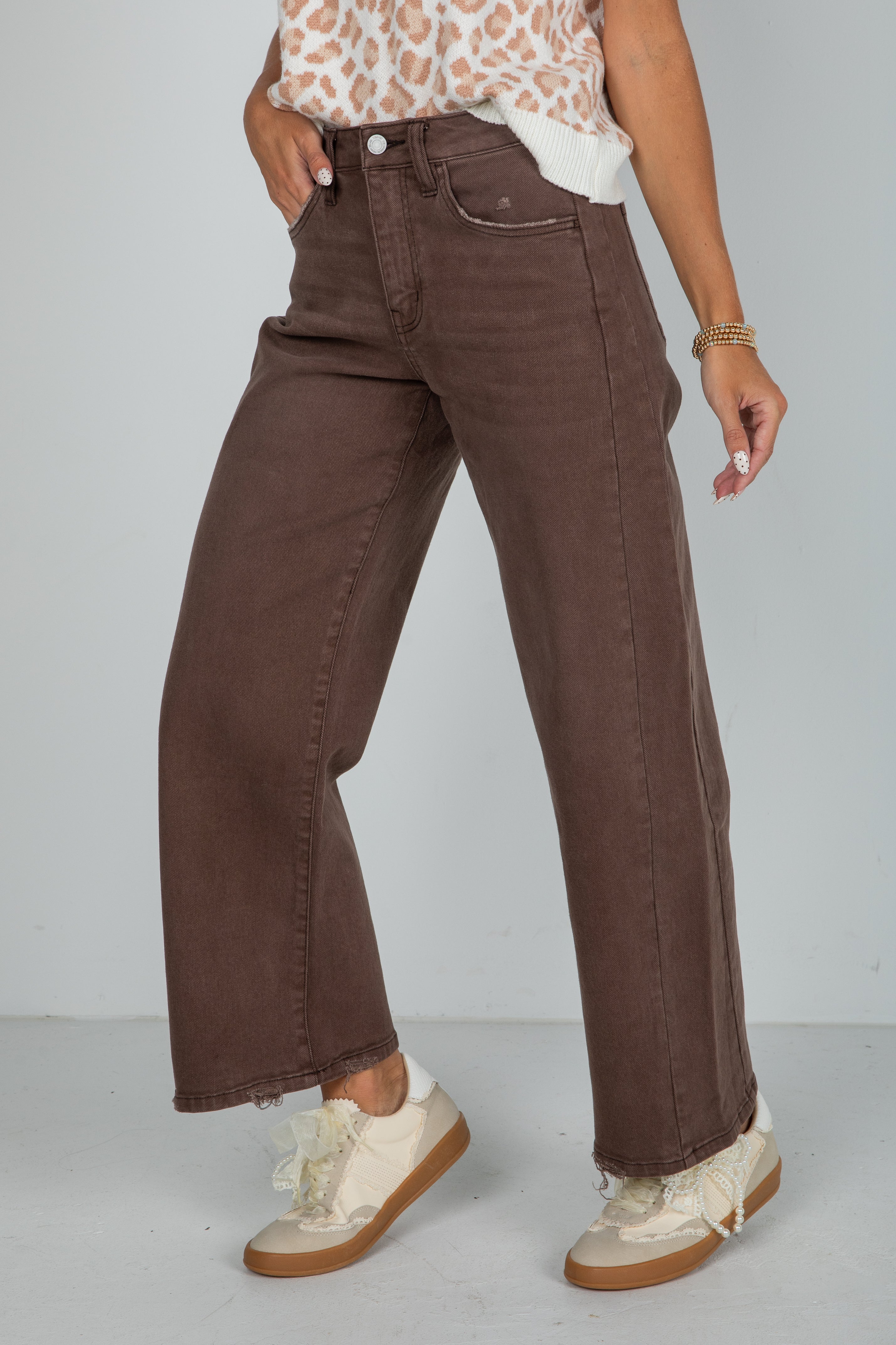 Person wearing brown wide-leg jeans and white sneakers on a plain background