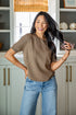 Woman in a brown sweater and blue jeans standing in a kitchen.