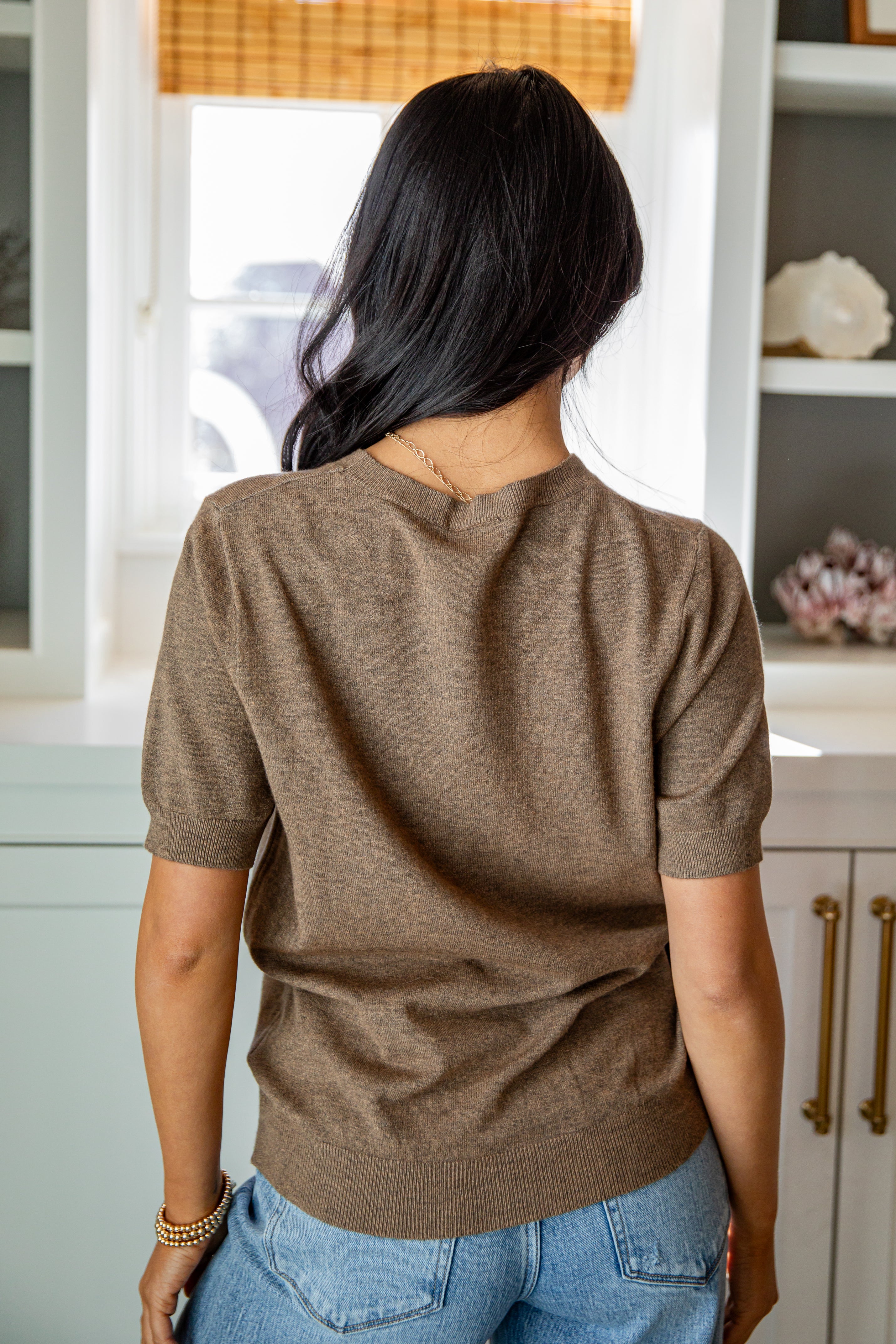 Person wearing a brown sweater and blue jeans in a kitchen setting