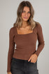 Woman wearing a brown ribbed sweater against a plain background