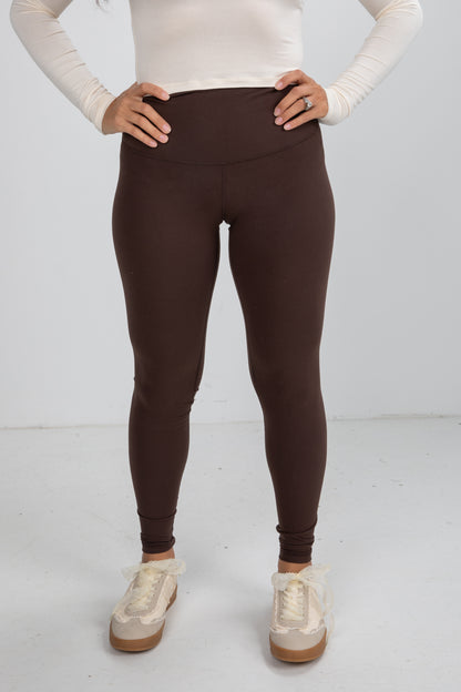 Person wearing brown leggings and white sneakers on a white background