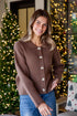 Woman wearing a brown ribbed sweater with white buttons in front of a decorated Christmas tree.
