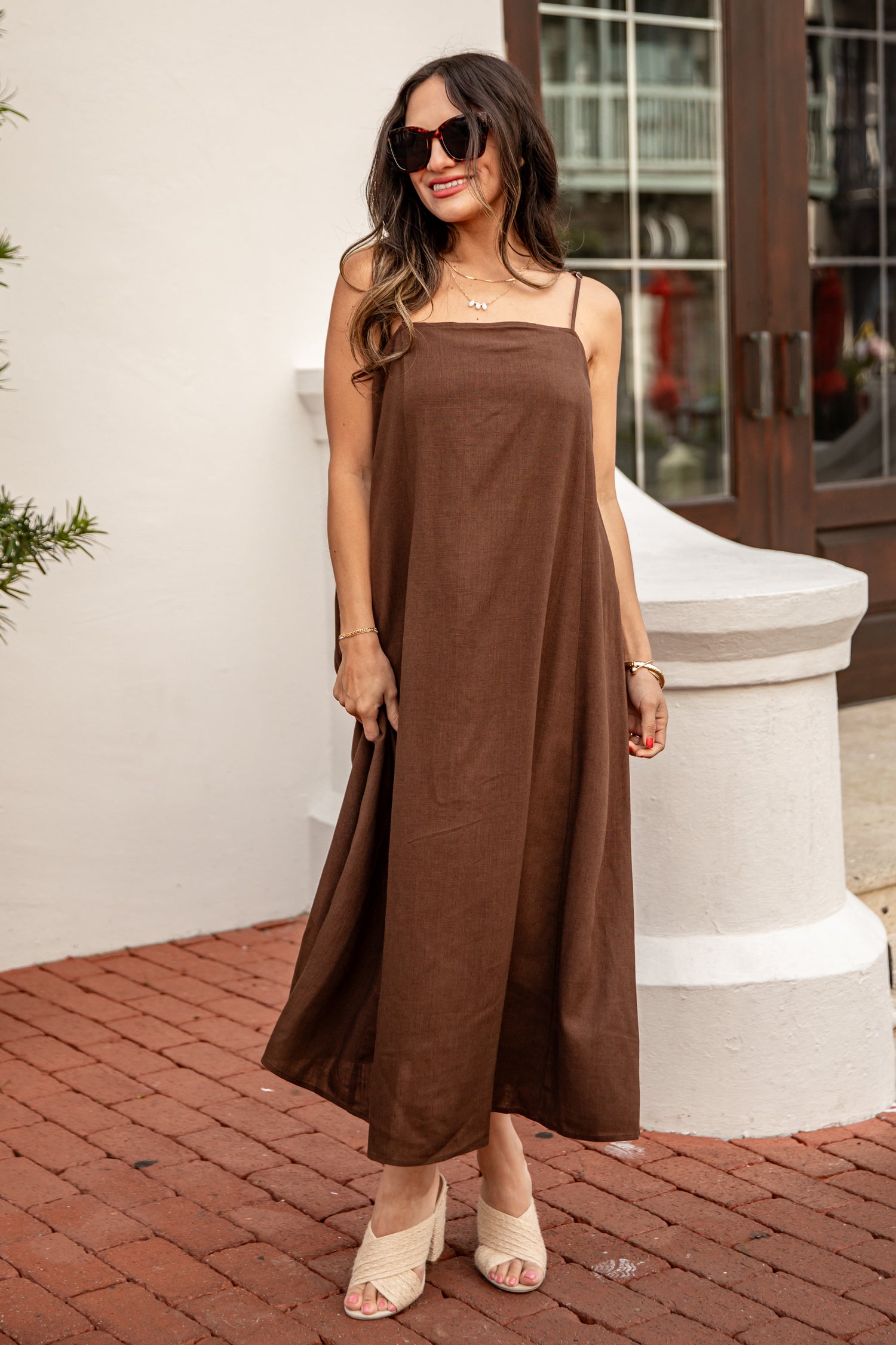 Woman wearing a brown slip dress standing on a brick patio.