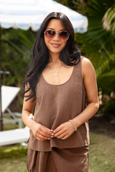 Woman wearing sunglasses and a brown sleeveless top and pants outdoors.