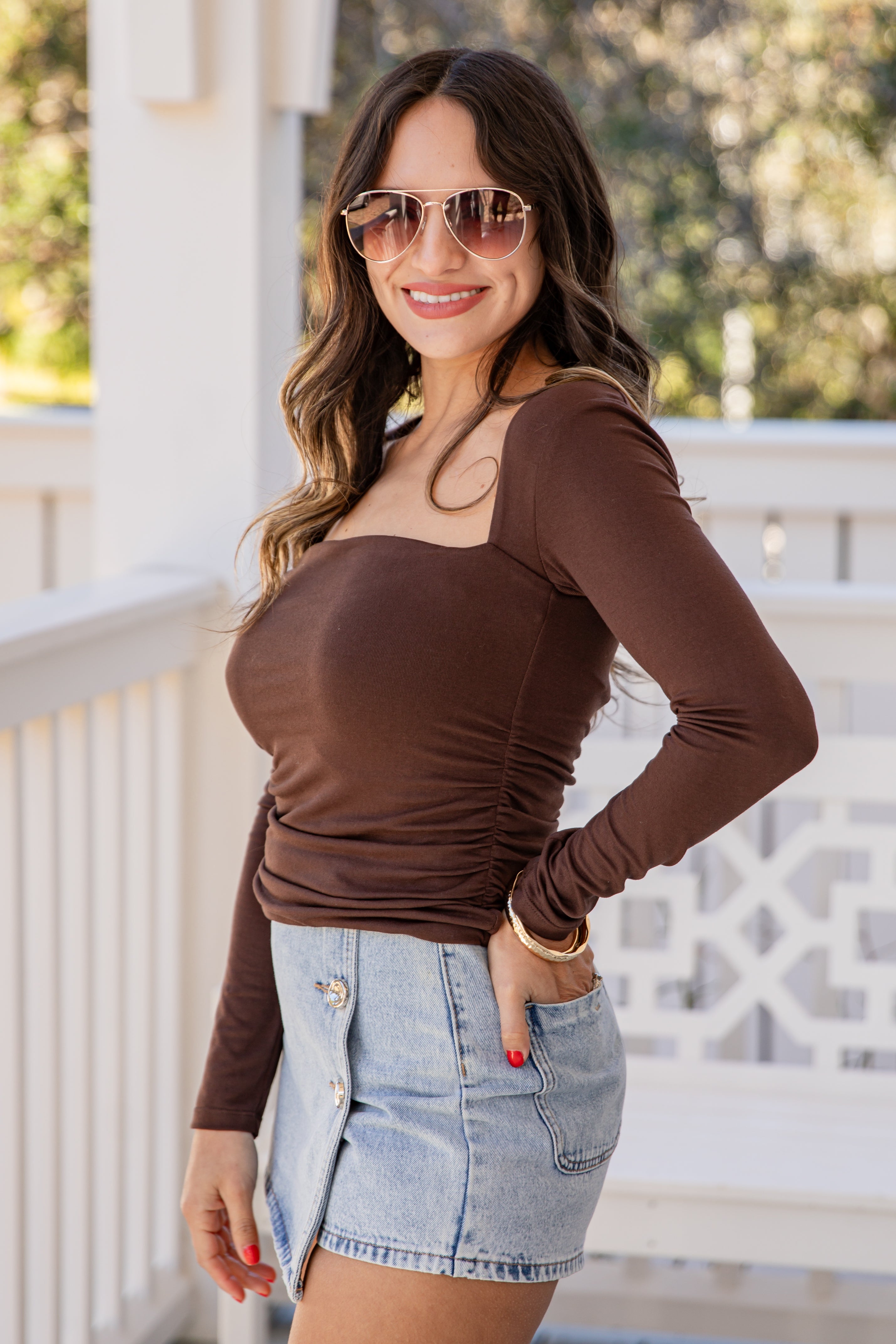 Woman wearing a brown long-sleeve top and denim shorts on a balcony.
